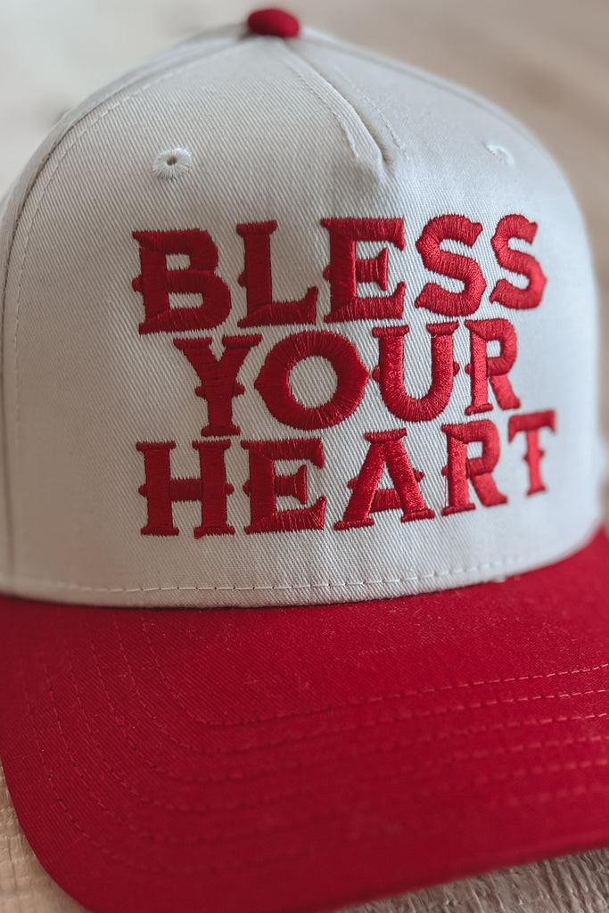 Red and white cap with 'Bless Your Heart' text on a beige background