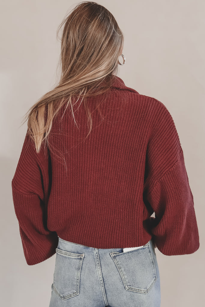 Person wearing a red sweater and light blue jeans against a beige background