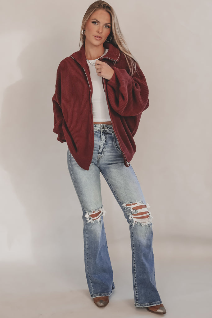 Woman wearing a burgundy jacket and ripped jeans on a plain background