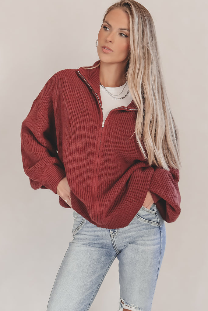 Woman wearing a red sweater and light blue jeans against a plain background