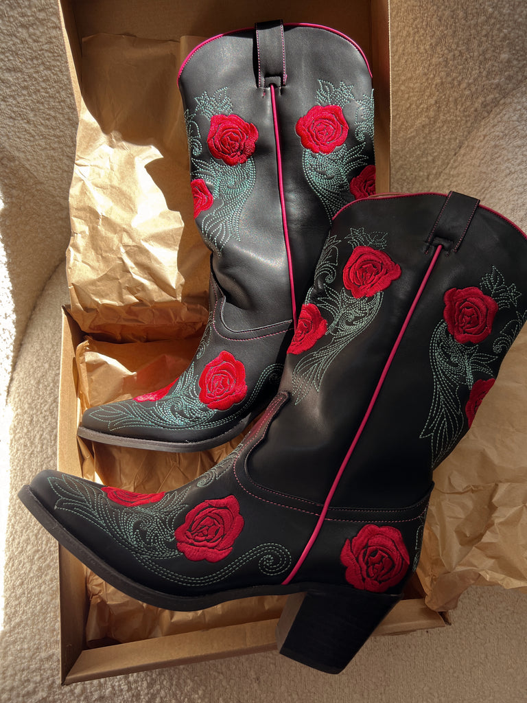Black cowboy boots with red rose designs in a cardboard box.