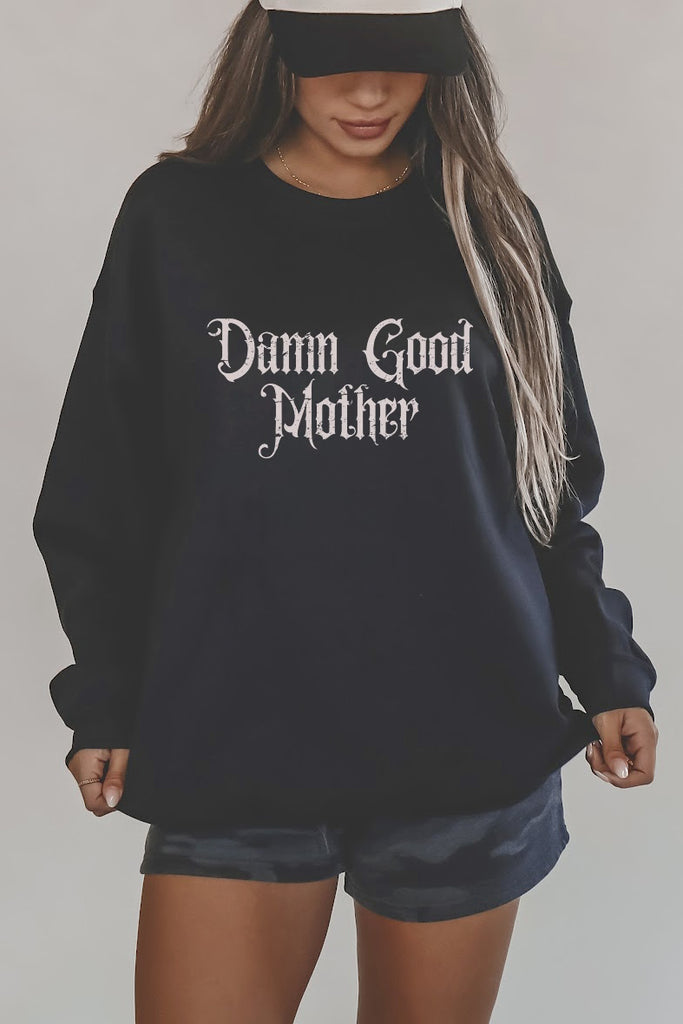 Person wearing a black sweatshirt with 'Damn Good Mother' text on a plain background