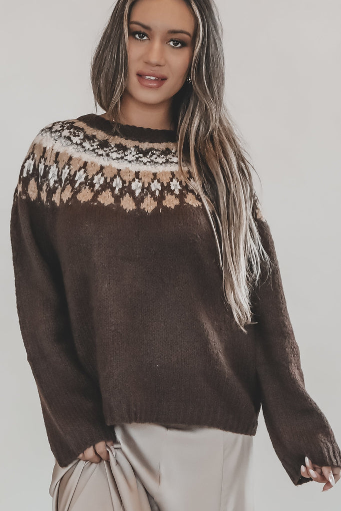 Woman wearing a brown sweater with a patterned neckline against a plain background