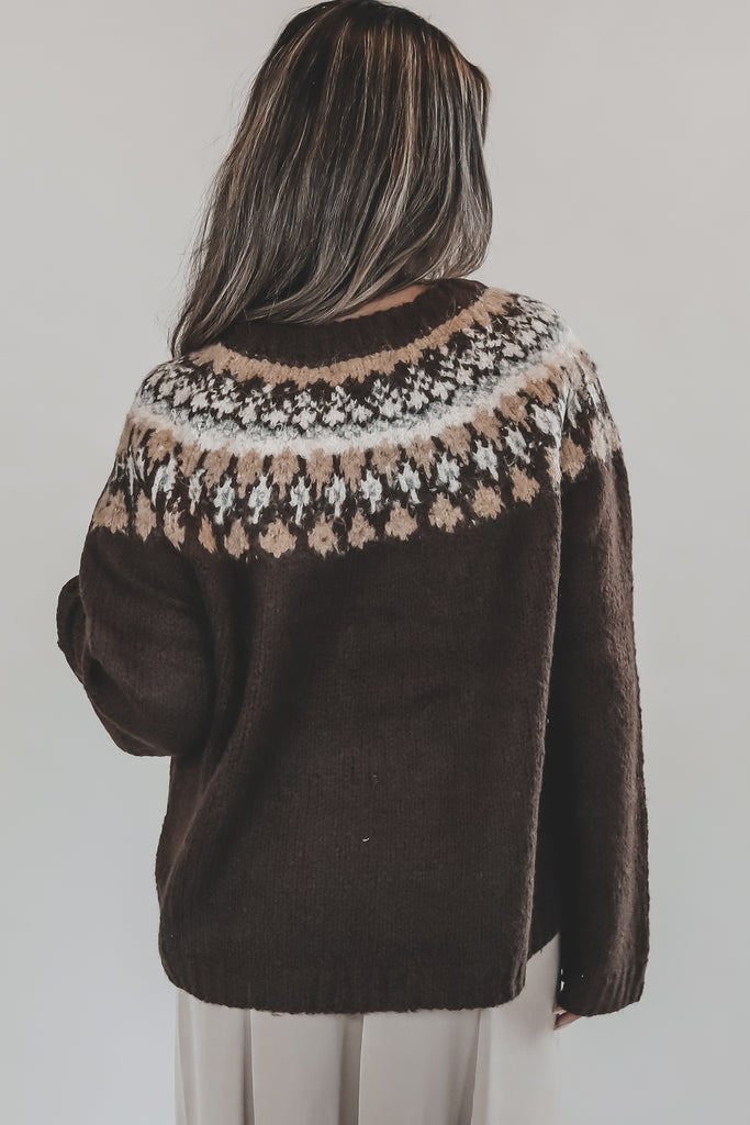 Person wearing a brown sweater with a patterned neckline against a white background