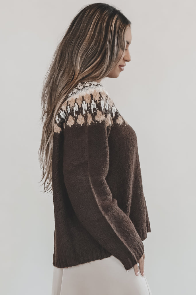Woman wearing a brown knitted sweater with a patterned yoke against a plain background