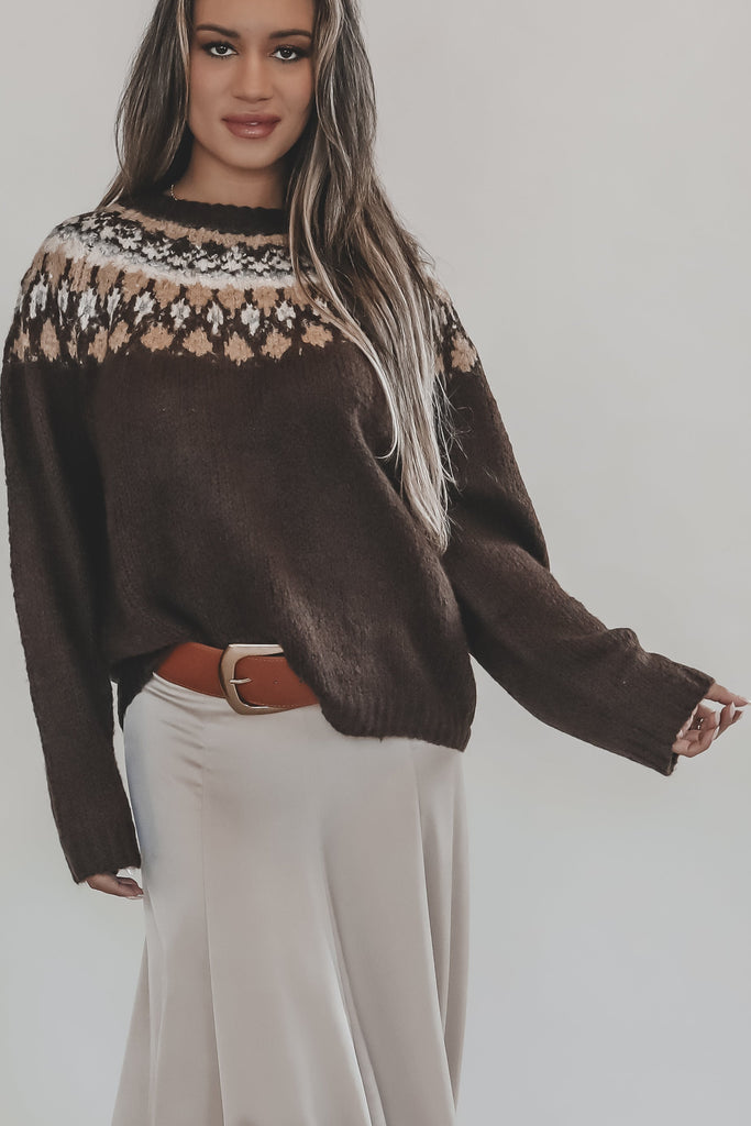 Woman wearing a brown sweater with a patterned neckline and a beige skirt on a white background