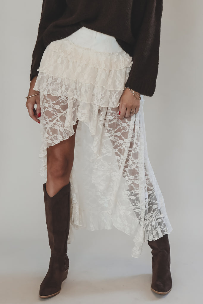 Person wearing a white lace skirt and brown boots on a plain background