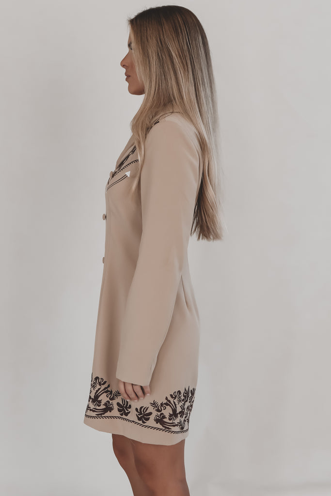 Woman wearing a beige dress with black embroidery on a plain background