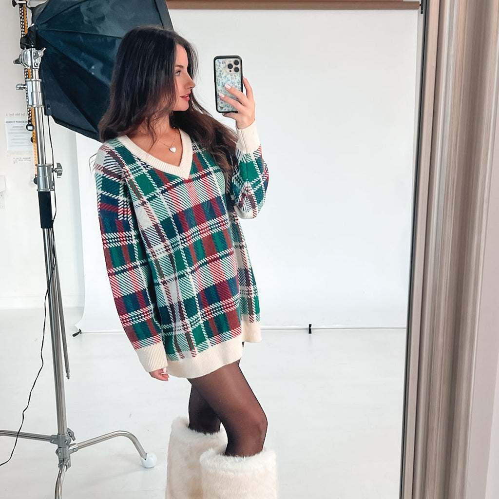 Woman taking a mirror selfie wearing a plaid dress in a studio setting.
