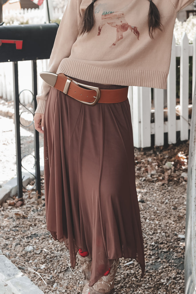 Person wearing a beige sweater with a deer design and a brown skirt outdoors.