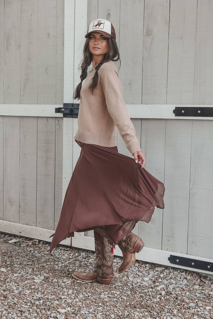 Woman in a beige sweater and brown skirt standing in front of a wooden door.