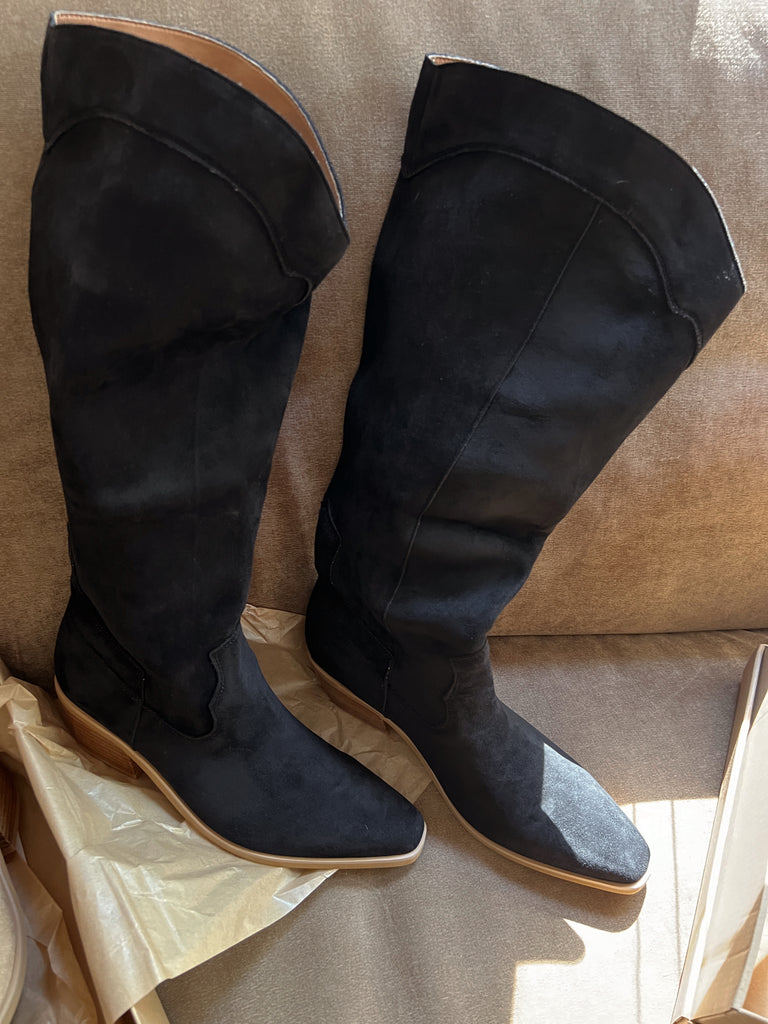 Black knee-high boots on a beige surface with a neutral background
