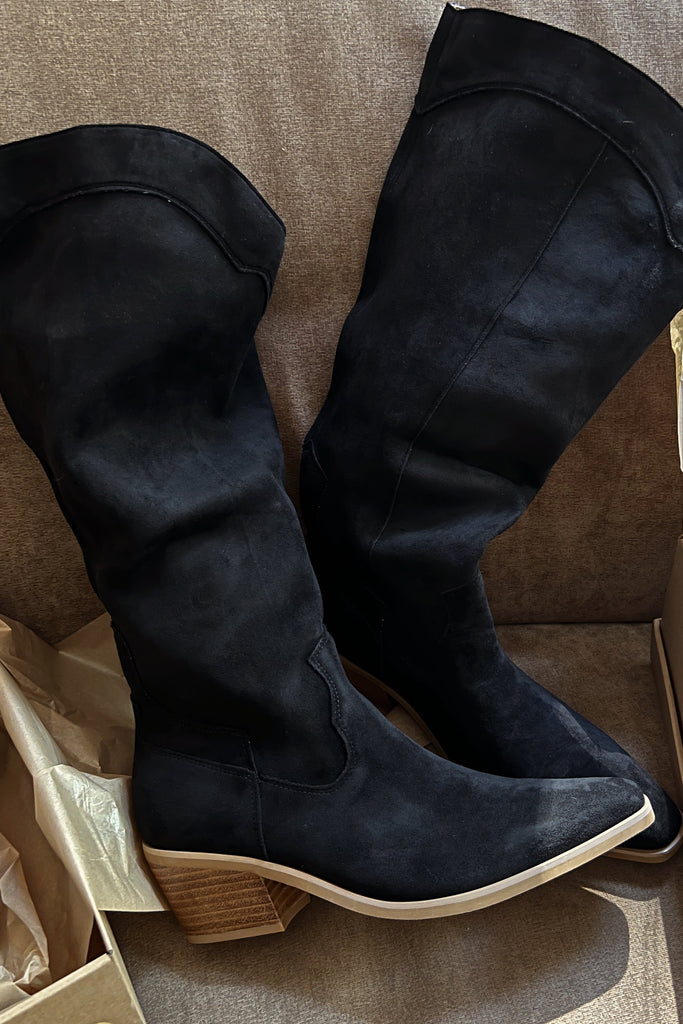 Black knee-high boots with wooden heel on a beige surface